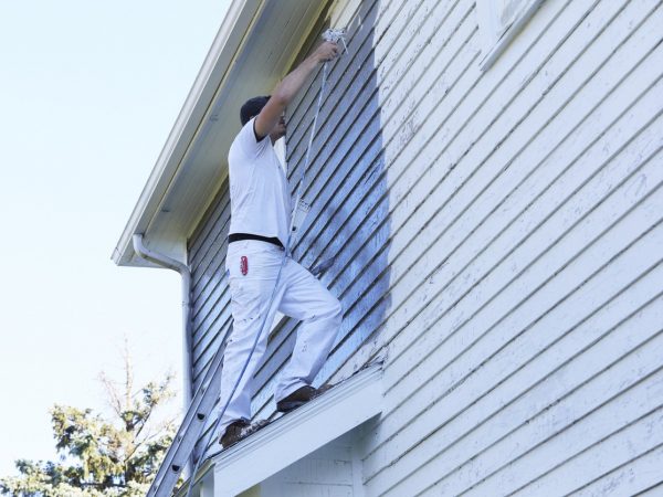 Man Spraying Paint On Exterior of Old Home